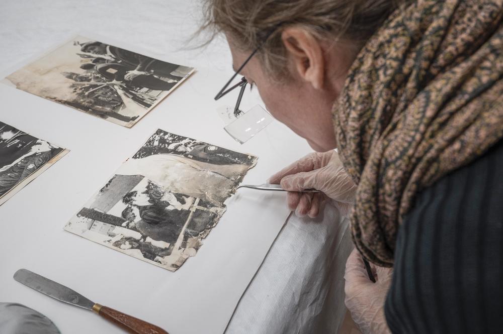 Photo restorer Stefanie Pfeifer is shown at work with tweezers. It is the first step in preparing the photographs for digitization in order to make them accessible to interested individuals.