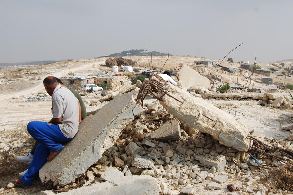 Two men are sitting on the ruins of their village’s mosque. Israel Defense Forces destroyed it because Palestinians built it without a building permit. They couldn’t get a permit because the area was declared a military zone.