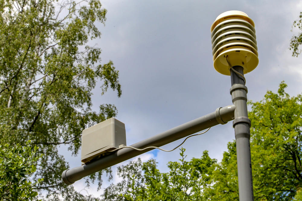 A measuring device consisting of a passively ventilated device with sensors for detecting temperature, humidity, pressure, radiation, and solar cells as well as a rechargeable battery (at right) and rain gauge (at left).